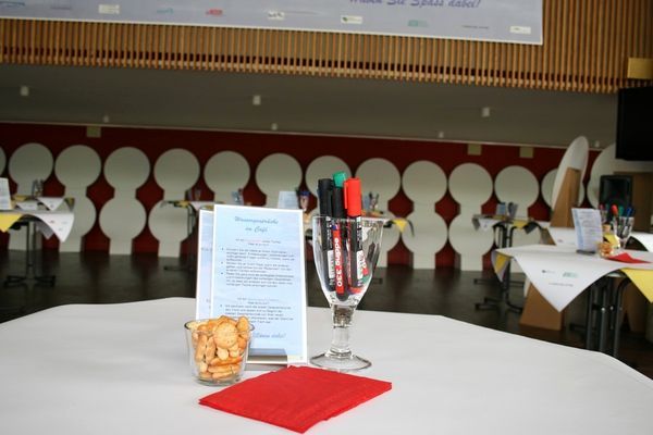 Vorbereiteter Workshop-Tisch mit Moderationsstiften, Snacks und Info-Karte in hellem Seminarraum